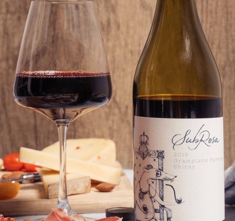 open bottle of the subrosa grampians pyrenees shiraz with a glass next to it and cheese in the background