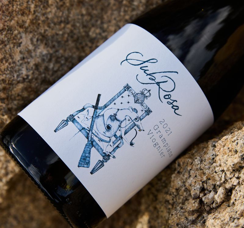 Bottle of Subrosa Viognier wine placed on the rocks. The vineyard is comprised of rocky soil.