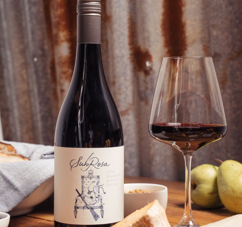 Subrosa shiraz malakoff estate bottle and glass of red wine on a table with charcuterie for pairing