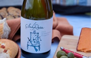bottle of subrosa grampians viognier on the table with pairing ideas like cheese and olives around it