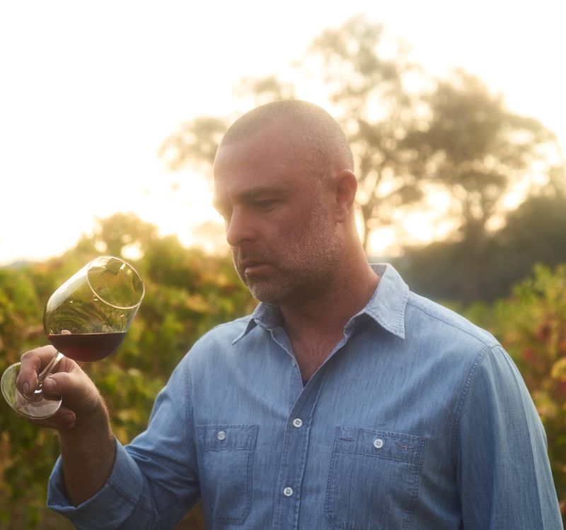 adam louder, subrosa winemaker looking at a glass of the subrosa 2021 shiraz while in the grampians vineyard