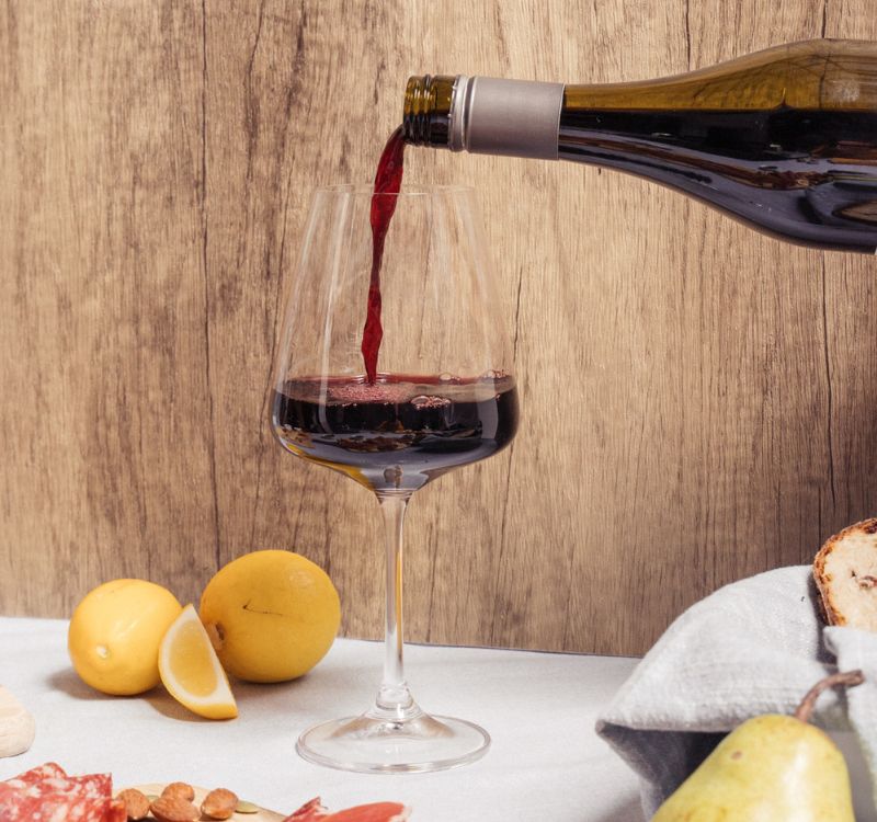 a glass of subrosa 2021 grampians shiraz being poured on a table with foods to pair like nuts and cheese